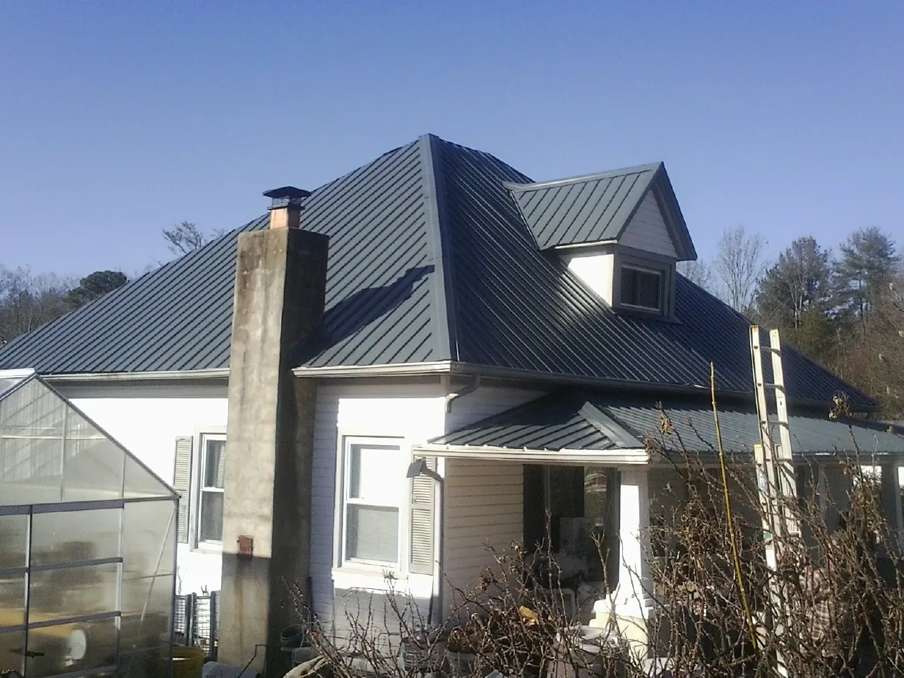 Dark blue standing seam metal roof on a white farmhouse with dormer — Slate & Tile Roof Repair by Roofing Brothers in Canton