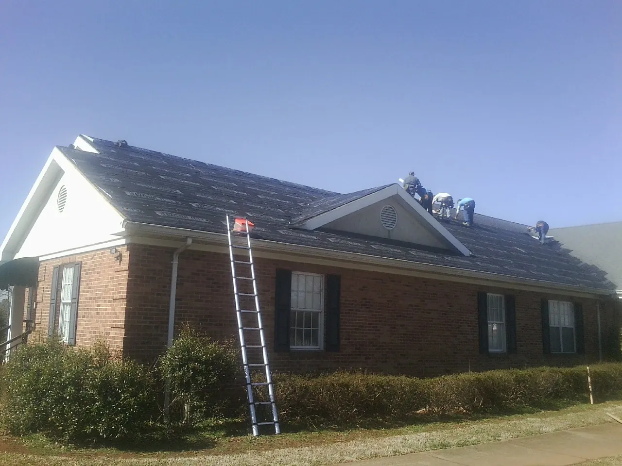 Crew tearing shingles off a brick ranch roof with a ladder set — Emergency Roof Repair work by our crew in Canton