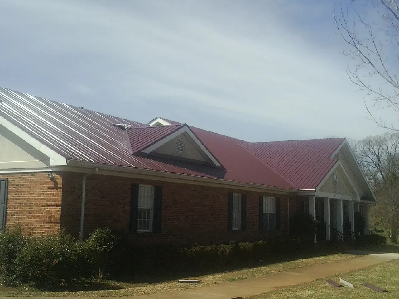 Red metal roof with gabled entries on a long brick building, from a Hail Damage Roof Repair job in Canton